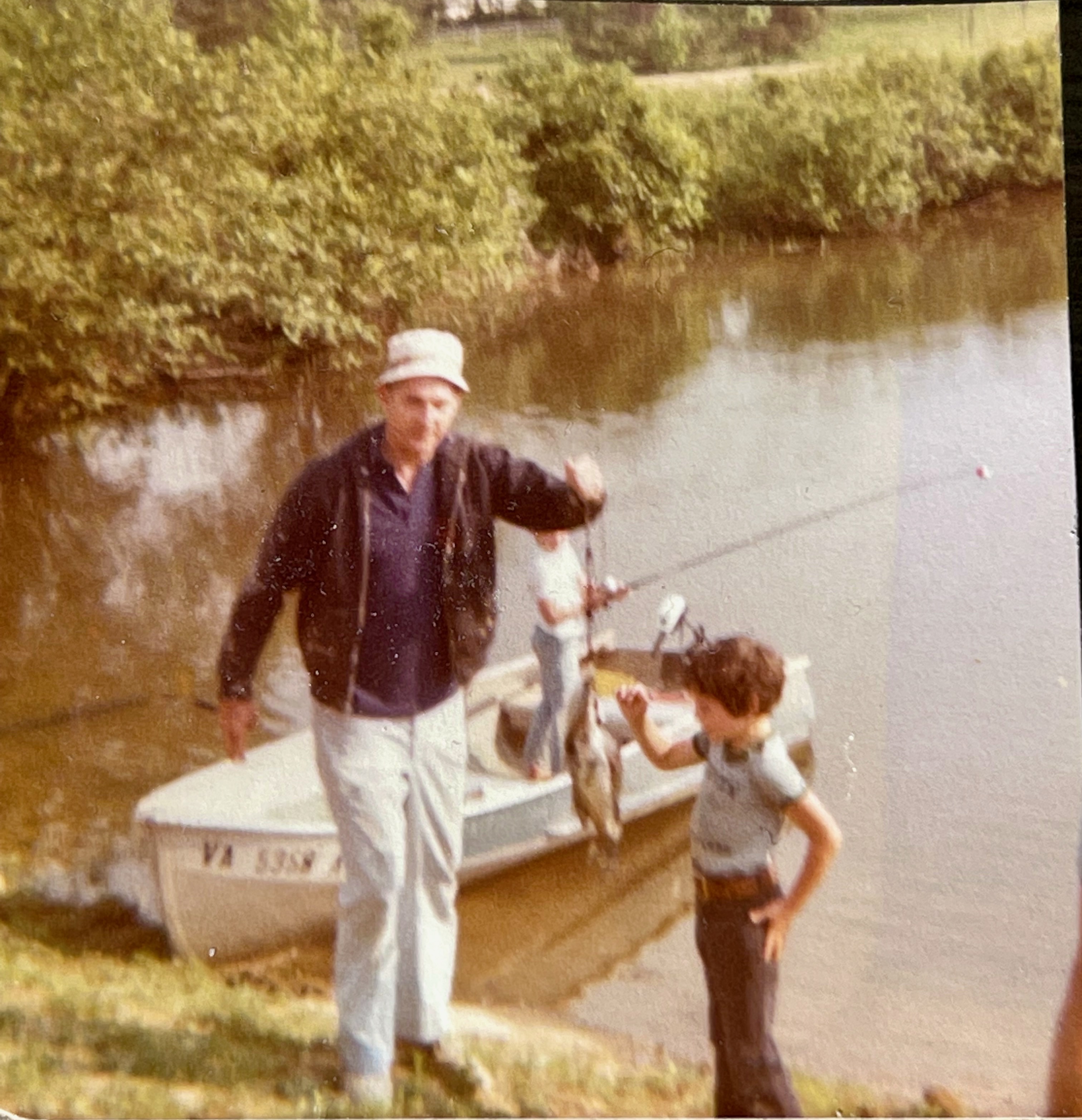 Don McCool and a young Jim fishing by a boat at the water's edge.
