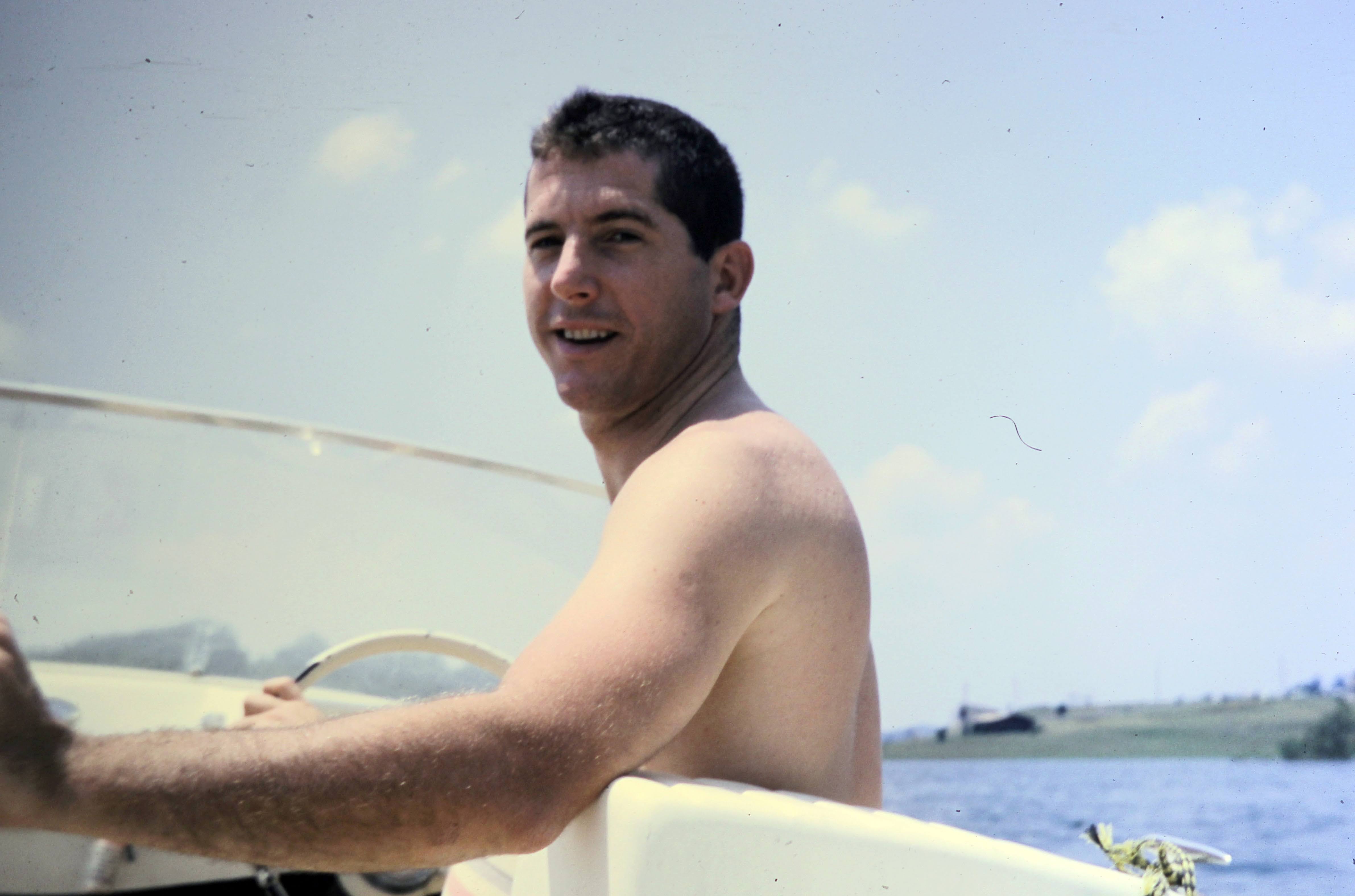 A young Don McCool at the wheel of a boat on the water.